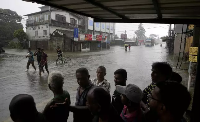 People takes shelter as it rains while others wade through a flooded street in Colombo, Sri Lanka, Sunday, Oct. 13, 2024. (AP Photo/Eranga Jayawardena)