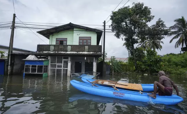 A man sits on a catamaran next to a damaged house in a flooded area in Colombo, Sri Lanka, Monday, Oct. 14, 2024. (AP Photo/Eranga Jayawardena)