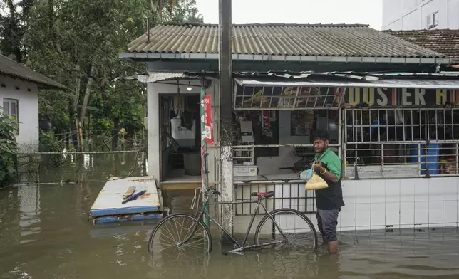 A man buys groceries in his flooded neighborhood in Colombo, Sri Lanka, Monday, Oct. 14, 2024. (AP Photo/Eranga Jayawardena)