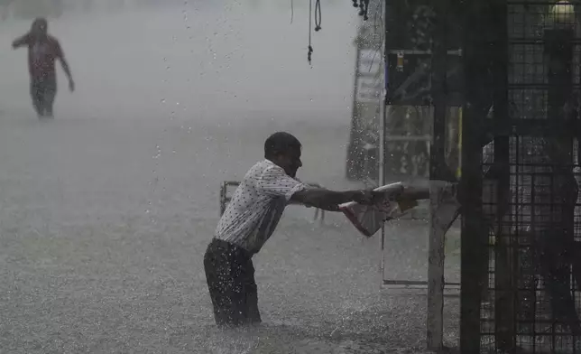 A man reaches for a safe place as it rains in a flooded street in Colombo, Sri Lanka, Sunday, Oct. 13, 2024. (AP Photo/Eranga Jayawardena)