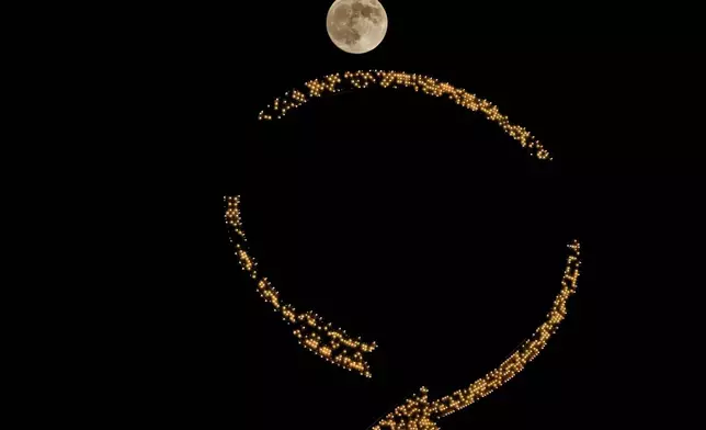 The moon rises beyond an antique sign atop a downtown apartment building, Wednesday, Oct. 16, 2024, in Kansas City, Mo. (AP Photo/Charlie Riedel)