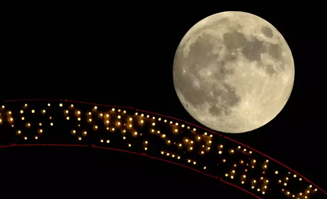 The moon rises beyond an antique sign atop a downtown apartment building, Wednesday, Oct. 16, 2024, in Kansas City, Mo. (AP Photo/Charlie Riedel)