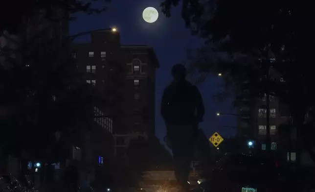 The full moon rises as a person cruises down a street on an electric scooter Wednesday, Oct. 16, 2024, in Chicago. (AP Photo/Kiichiro Sato)