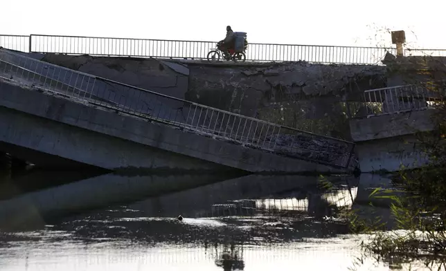 A man on his motorcycle passes by a bridge that links to Lebanon which was destroyed on Oct. 24 by an Israeli airstrike, in Qusair, Syria, Sunday, Oct. 27, 2024. (AP Photo/Omar Sanadiki)