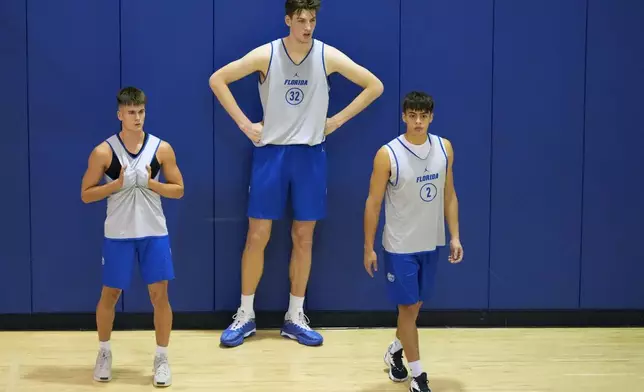 Olivier Rioux, center, a 7-foot-9 NCAA college basketball player at Florida, takes a break at practice with teammates Kajus Kublickas, left, and Kevin Pazmino (2), Friday, Oct. 18, 2024, in Gainesville, Fla. (AP Photo/John Raoux)