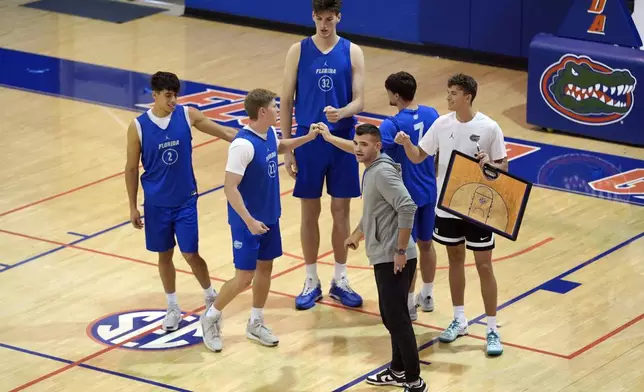 Olivier Rioux, back center, a 7-foot-9 NCAA college basketball player at Florida, gathers with coaches and teammates at the team's practice, Friday, Oct. 18, 2024, in Gainesville, Fla. (AP Photo/John Raoux)