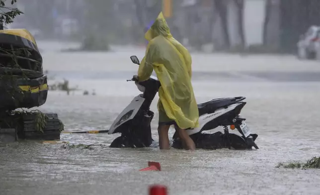 A man pushes a motorbike through a flooded road as Typhoon Krathon makes landfall in Kaohsiung, southern Taiwan, Thursday, Oct. 3, 2024. (AP Photo/Chiang Ying-ying)