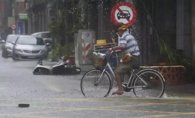 A man pedals through a flooded road as Typhoon Krathon makes landfall in Kaohsiung, southern Taiwan, Thursday, Oct. 3, 2024. (AP Photo/Chiang Ying-ying)