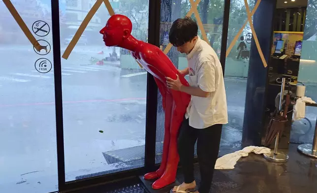 A hotel staff prepares to move a human figure from the doorway to inside as Typhoon Krathon arrives in Kaohsiung, southern Taiwan, Thursday, Oct. 3, 2024. (AP Photo/Chiang Ying-ying)