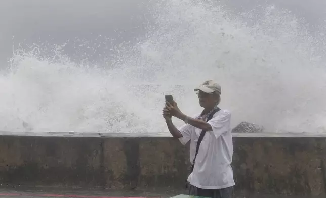 A man takes a selfie with waves hitting the shore of Kaohsiung, southern Taiwan, Wednesday, Oct. 2, 2024, as Typhoon Krathon is expected to hit the area. (AP Photo/Chiang Ying-ying)