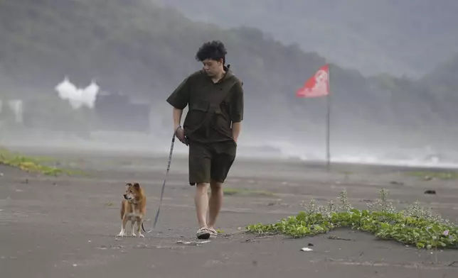 A man walks his dog on a beach as Typhoon Krathon approaches to Taiwan in Yilan County, eastern coast of Taiwan, Tuesday, Oct. 1, 2024. (AP Photo/Chiang Ying-ying)