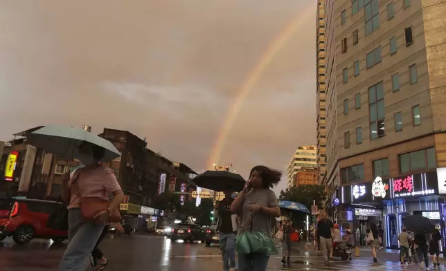 People walk in the rain with a backdrop of the rainbow in the sky as Typhoon Krathon approaches to Taiwan in Taipei, Monday, Sept. 30, 2024. (AP Photo/Chiang Ying-ying)