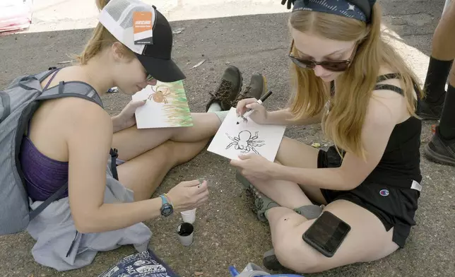 Kendall Foreman, left, and Raven Myhre, right, both of Fort Collins, Colo., create artwork at the Tarantula Festival in La Junta, Colo., on Saturday, Sept. 28, 2024. (AP Photo/Thomas Peipert)