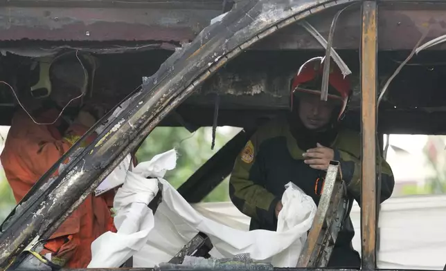 Rescuers hold a white cloth to cover the body of a victim inside a bus that caught fire, carrying young students with their teachers, in suburban Bangkok, Tuesday, Oct. 1, 2024. (AP Photo/Sakchai Lalit)