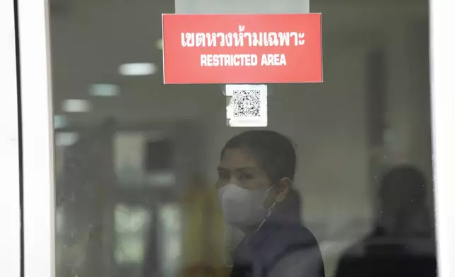 A forensic officer stands behind the forensic department at a police hospital in Bangkok, Thailand, Wednesday, Oct. 2, 2024, as family members of victims visit there after a bus carrying students and teachers caught a fire Tuesday. (AP Photo/Sakchai Lalit)