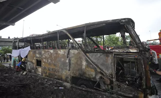 A rescuer inspects a bus that caught fire, carrying young students with their teachers, in suburban Bangkok, Tuesday, Oct. 1, 2024. (AP Photo/Sakchai Lalit)