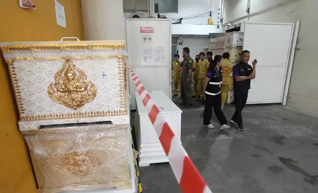 Forensic officers stand beside empty coffins at a forensic police hospital in Bangkok, Thailand, Wednesday, Oct. 2, 2024, following a deadly bus fire incident. (AP Photo/Sakchai Lalit)