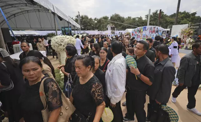 People stand in a queue to offer their final respects at the cremation for victims of a school bus fire, at Wat Khao Phraya Sangkharam School, Lan Sak, Uthai Thani province, Thailand, Tuesday, Oct. 8, 2024. (AP Photo/Chatkla Samnaingjam)