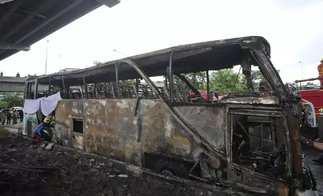 A rescuer inspects a bus that caught fire, carrying young students with their teachers, in suburban Bangkok, Tuesday, Oct. 1, 2024. (AP Photo/Sakchai Lalit)