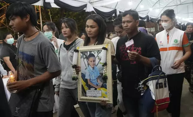 Victims' relatives carry portraits of the victims of a bus fire in a procession at Wat Khao Phraya Sangkharam School Lan Sak , Uthai Thani province, Thailand, Thursday, Oct. 3, 2024. (AP Photo/Sakchai Lalit)