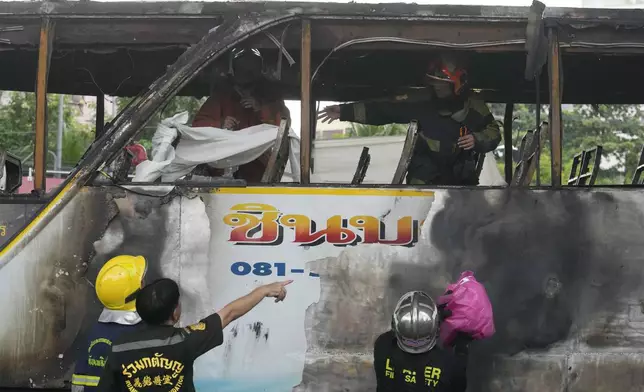 Rescuers hold a white cloth to cover the body of a victim inside a bus that caught fire, carrying young students with their teachers, in suburban Bangkok, Tuesday, Oct. 1, 2024. (AP Photo/Sakchai Lalit)