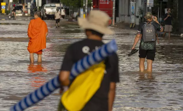 People and a Buddhist monk wade through floodwaters in Chiang Mai Province, Thailand, Sunday, Oct. 6, 2024 as the city's main river overflowed its banks following heavy seasonal rainfall. (AP Photo/Wason Wanichakorn)