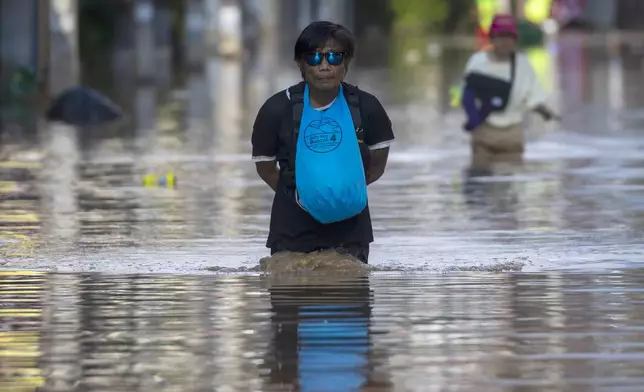 People hang their belongings around neck through floodwaters in Chiang Mai Province, Thailand, Sunday, Oct. 6, 2024 as the city's main river overflowed its banks following heavy seasonal rainfall. (AP Photo/Wason Wanichakorn)