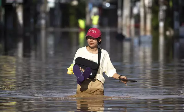 A woman wades through floodwaters in Chiang Mai Province, Thailand, Sunday, Oct. 6, 2024 as the city's main river overflowed its banks following heavy seasonal rainfall. (AP Photo/Wason Wanichakorn)