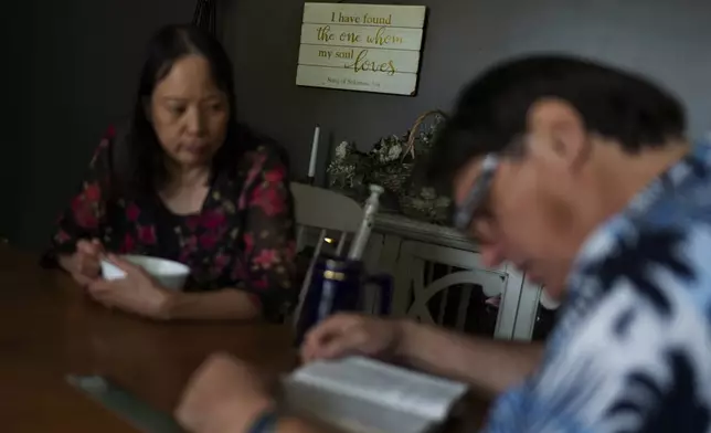 A message decorates the wall behind Lesley, left, and Matt Dzik, as they read the Bible at their home in Champaign, Ill., Sunday, Sept. 22, 2024. When they came across Braver Angels, a nonprofit that helps people bridge the political divide, they found a community there that is both red and blue. "It gave me enough hope," said Lesley. "I felt safe, I'm not alone." (AP Photo/David Goldman)