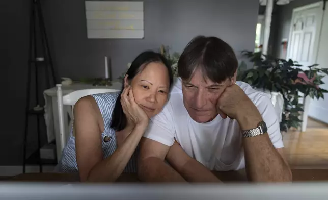 Lesley, left, and Matt Dzik, watch a seminary studies presentation by Lesley's son on a laptop in their home in Champaign, Ill., Friday, Sept. 20, 2024. When they started dating, all it took was the sight of Democratic lawn signs outside Matt's house ahead of the 2020 election to make Lesley question if their relationship could work. (AP Photo/David Goldman)