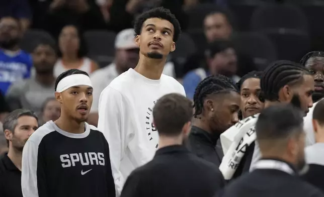 San Antonio Spurs center Victor Wembanyama, center, watches from the bench during the first half of a preseason NBA basketball game against the Oklahoma City Thunder in San Antonio, Monday, Oct. 7, 2024. (AP Photo/Eric Gay)