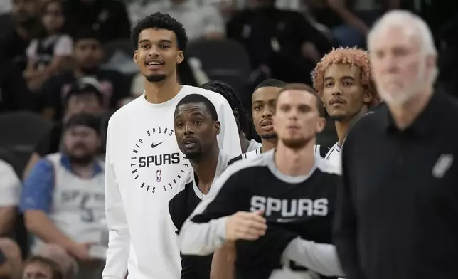 San Antonio Spurs center Victor Wembanyama, left, watches from the bench during the second half of a preseason NBA basketball game against the Oklahoma City Thunder in San Antonio, Monday, Oct. 7, 2024. (AP Photo/Eric Gay)