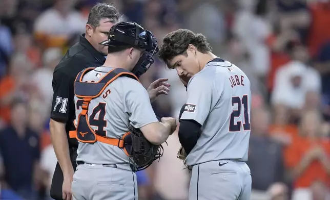 Detroit Tigers catcher Jake Rogers (34) and relief pitcher Jackson Jobe (21) work on Jobe's communications device as home plate umpire Jordan Baker (71) looks on in the seventh inning of Game 2 of an AL Wild Card Series baseball game Wednesday, Oct. 2, 2024, in Houston. (AP Photo/Kevin M. Cox)