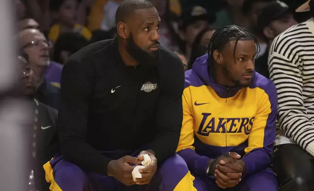 Los Angeles Lakers forward LeBron James guard Bronny James watch play during the first half of an NBA basketball game against the Minnesota Timberwolves, Tuesday, Oct. 22, 2024, in Los Angeles. (AP Photo/Eric Thayer)