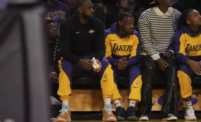 Los Angeles Lakers forward LeBron James (23) guard Bronny James watch play during the first half of an NBA basketball game against the Minnesota Timberwolves, Tuesday, Oct. 22, 2024, in Los Angeles. (AP Photo/Eric Thayer)