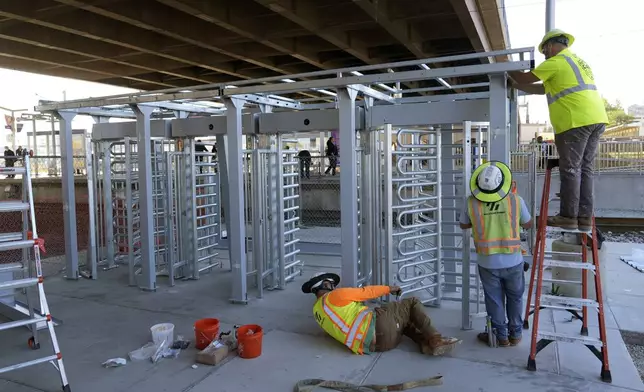 Workers install a metal gate that will prevent customers from entering a MetroLink platform without a valid fare card in an effort to increase security Wednesday, Oct. 9, 2024, in St. Louis. (AP Photo/Jeff Roberson)