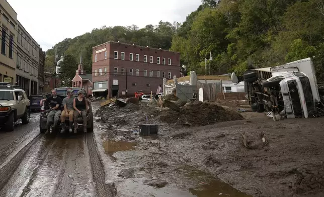 People ride in the back of a pickup truck on a mud-covered street left in the aftermath of Hurricane Helene, Tuesday, Oct. 1, 2024, in Marshall, N.C. (AP Photo/Jeff Roberson)