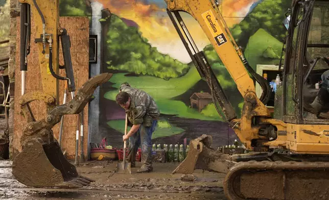 Heavy machinery passes by Bryson Effler, center, as he works to clear the sidewalk of mud left in the wake of Hurricane Helene, Tuesday, Oct. 1, 2024, in Marshall, N.C. (AP Photo/Jeff Roberson)