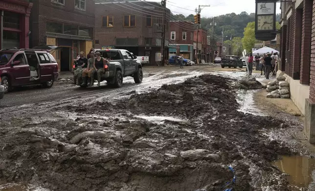 People ride in the back of a pickup truck on a street left covered in deep mud in the aftermath of Hurricane Helene Tuesday, Oct. 1, 2024, in Marshall, N.C. (AP Photo/Jeff Roberson)