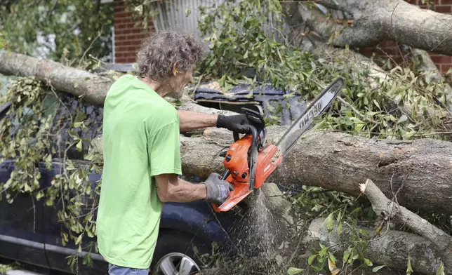 Andy Brown uses a chain saw to cut apart a tree that destroyed his SUV when it fell during Hurricane Helene on in Augusta, Ga., Tuesday, Oct. 1, 2024. (AP Photo/Jeffrey Collins)