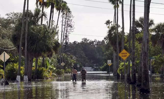 FILE - Men walk down a street flooded by Hurricane Helene in the Shore Acres neighborhood Sept. 27, 2024, in St. Petersburg, Fla. (AP Photo/Mike Carlson, File)