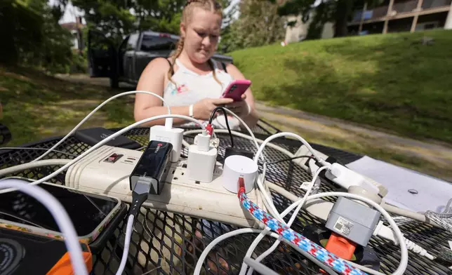 Carrie Owenby looks at her phone as a neighbor with power dropped an extension cord for neighbors who have no power in the aftermath of Hurricane Helene, Monday, Sept. 30, 2024, in Asheville, N.C. (AP Photo/Mike Stewart)