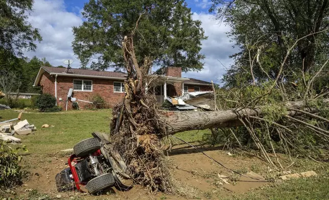 An overturned tractor lies next to an uprooted tree on the White family' property in the aftermath of Hurricane Helene, Tuesday, Oct. 1, 2024 in Morganton, N.C. The adjacent Catawba River flooded due to torrential rains destroying seven of the family's nine homes on the property. (AP Photo/Kathy Kmonicek)