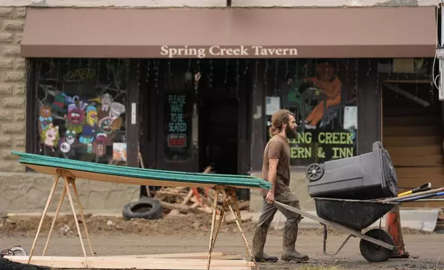 A person pushes a wheelbarrow and trash can as clean up in the aftermath of Hurricane Helene begins Tuesday, Oct. 1, 2024, in Hot Springs, N.C. (AP Photo/Jeff Roberson)