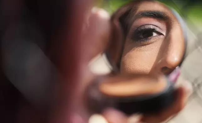 Julieth Luna Garcia, a transgender woman from El Salvador, looks into a compact mirror at Horner Park in Chicago, Monday, Sept. 30, 2024. (AP Photo/Nam Y. Huh)