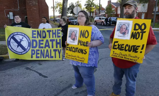 Jennifer Martin, center, and Thomas Roberson, right, older brother of condemned prisoner Robert Roberson, holds signs with others as they protest outside the prison where Roberson is scheduled for execution at the Huntsville Unit of the Texas State Penitentiary, Thursday, Oct. 17, 2024, in Huntsville, Texas. (AP Photo/Michael Wyke)