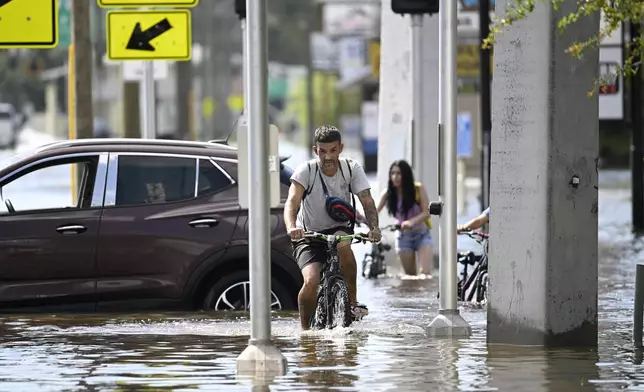 FILE - Mica Martell, left, and his niece and nephews ride bicycles through a flooded neighborhood, Sept. 27, 2024, in Crystal River, Fla. (AP Photo/Phelan M. Ebenhack, File)