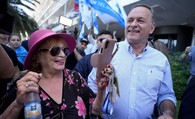 Alvaro Delgado, presidential candidate for the ruling National Party, walks alongside a supporter outside a polling station during general elections in Montevideo, Uruguay, Sunday, Oct. 27, 2024. (AP Photo/Natacha Pisarenko)