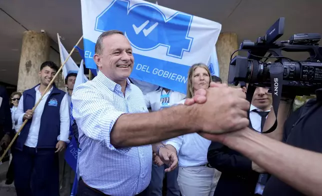 Alvaro Delgado, presidential candidate for the ruling National Party, center, greets a supporter outside a polling station during general elections in Montevideo, Uruguay, Sunday, Oct. 27, 2024. (AP Photo/Natacha Pisarenko)