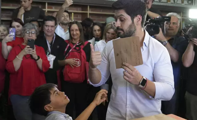 Andres Ojeda, Colorado Party presidential candidate, holds up his ballot while looking at his nephew at a polling station during general elections in Montevideo, Uruguay, Sunday, Oct. 27, 2024. (AP Photo/Matilde Campodonico)